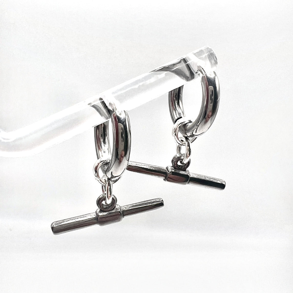 Mova silver tone T-bar hoop earrings hanging on a clear acrylic stand – Omasi Collection