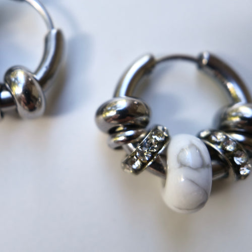Close-up of an Omasi Asteria huggie hoop earring in surgical steel, showing the white howlite stone between crystal rings