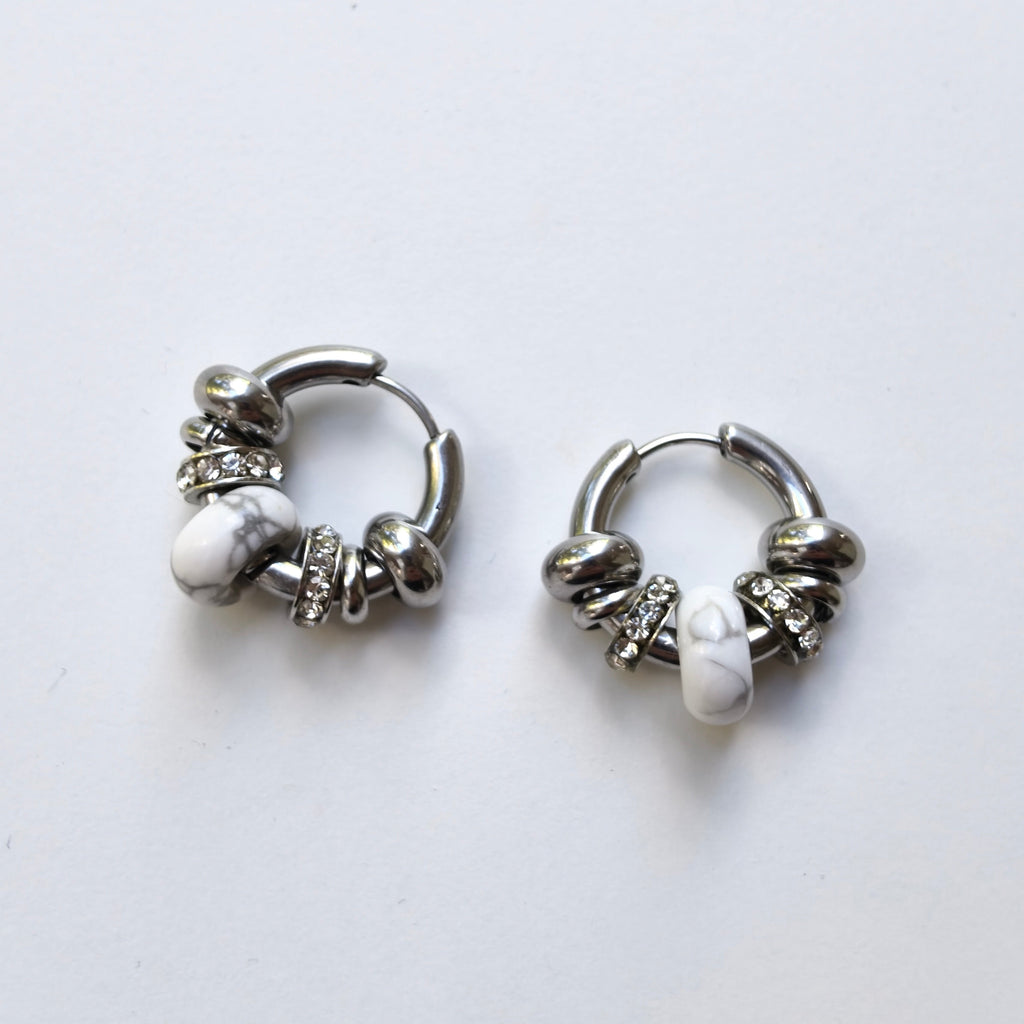 Pair of Omasi Asteria huggie hoop earrings in nickel-free surgical steel, each with a white howlite stone and crystal rings