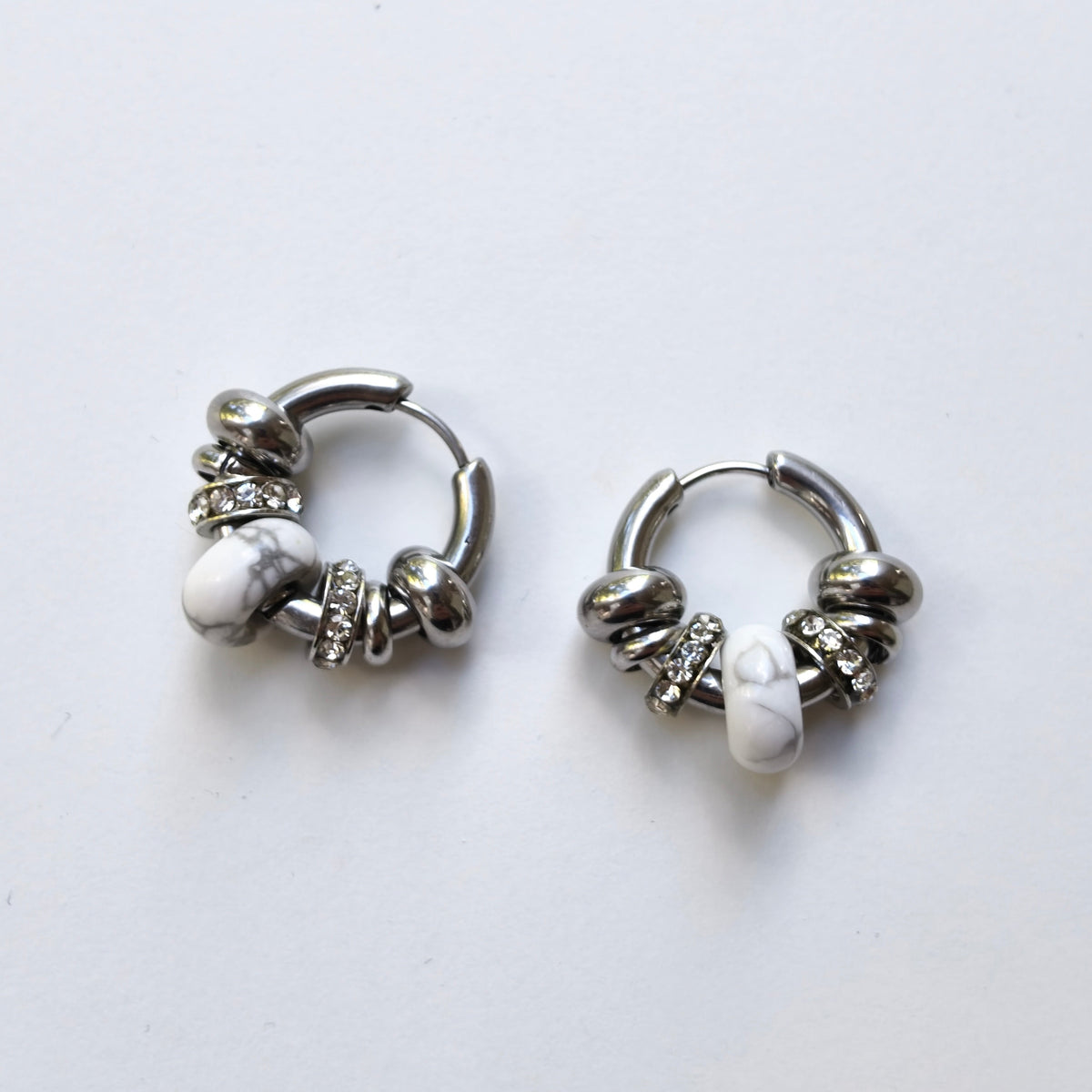 Pair of Omasi Asteria huggie hoop earrings in nickel-free surgical steel, each with a white howlite stone and crystal rings