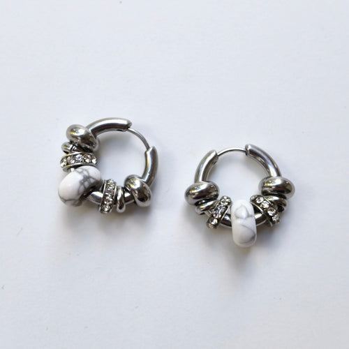 Pair of Omasi Asteria huggie hoop earrings in nickel-free surgical steel, each with a white howlite stone and crystal rings